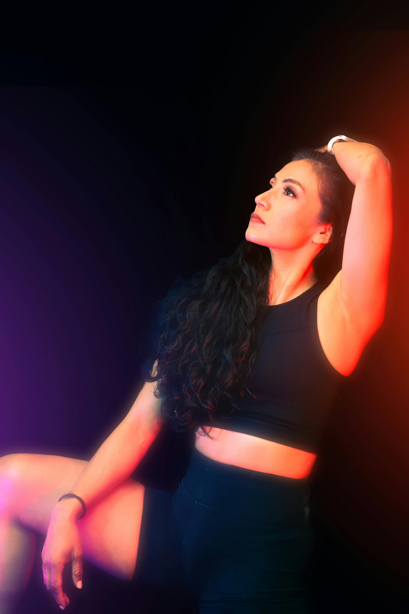 A striking portrait of a woman in activewear posing against a dark background with colorful lighting.