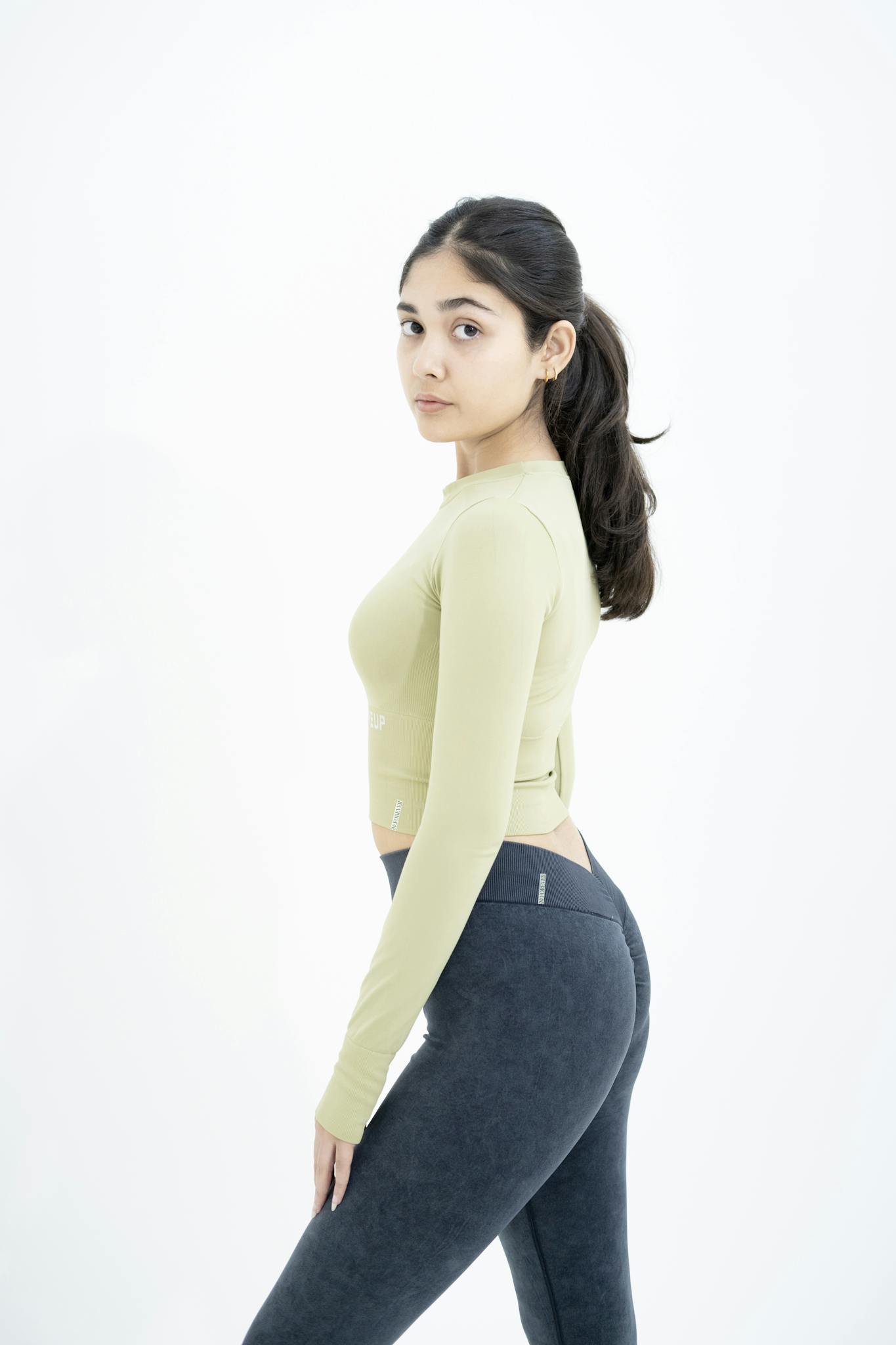 Confident young woman in trendy fitness outfit posing in minimalistic studio setting.