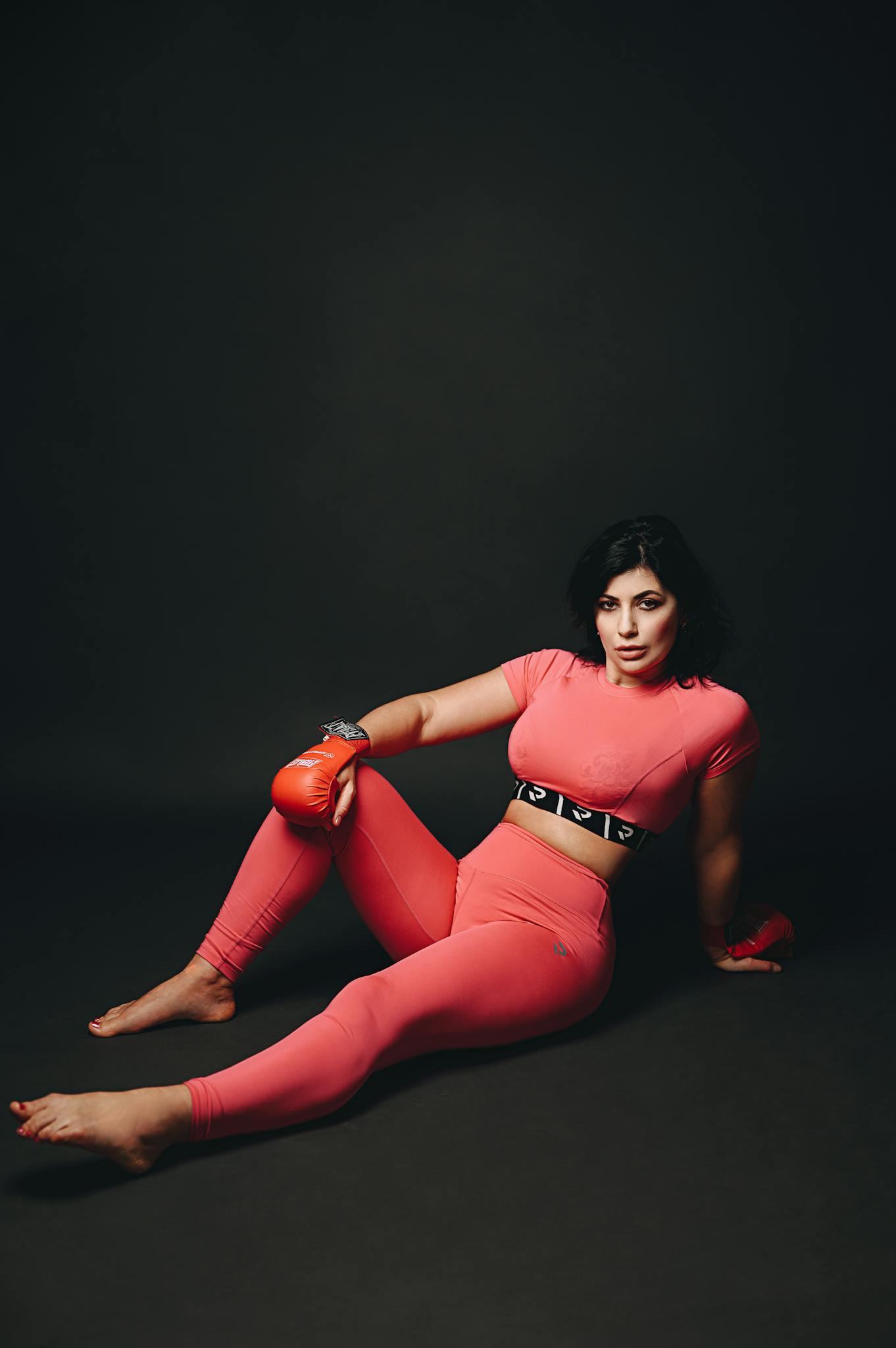 Model posing in studio with boxing gloves and vibrant sportswear, exuding strength and style.